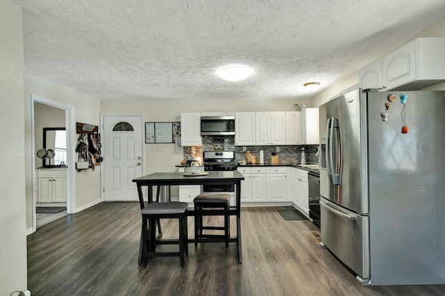 kitchen with white cabinetry, dark wood-type flooring, a textured ceiling, decorative backsplash, and appliances with stainless steel finishes