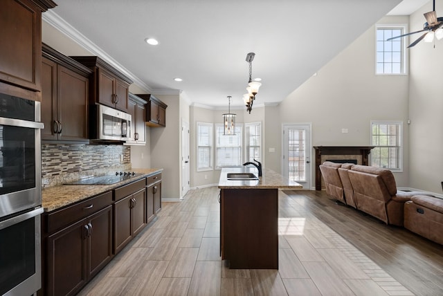 kitchen featuring black electric stovetop, light stone countertops, light wood-type flooring, an island with sink, and decorative light fixtures