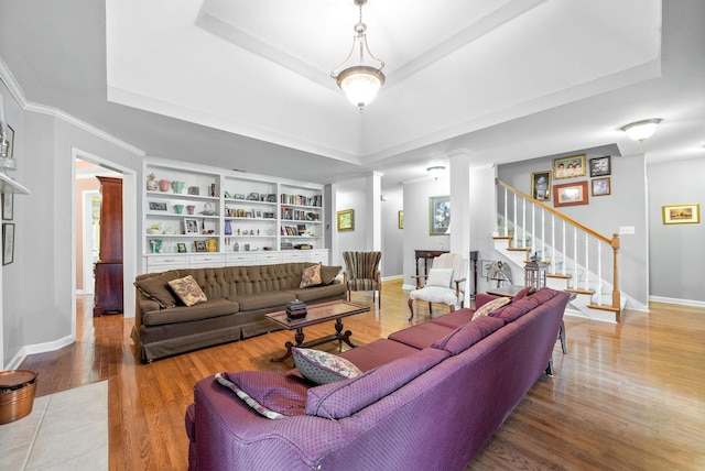 living room featuring hardwood / wood-style flooring, built in features, a tray ceiling, and ornate columns