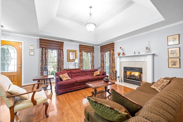 living room with a raised ceiling, ornamental molding, a fireplace, and light hardwood / wood-style flooring