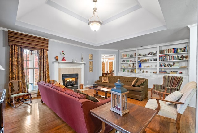 living room featuring a tray ceiling, light hardwood / wood-style flooring, ornamental molding, and a tiled fireplace