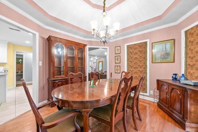 dining area with a tray ceiling, crown molding, an inviting chandelier, and light wood-type flooring