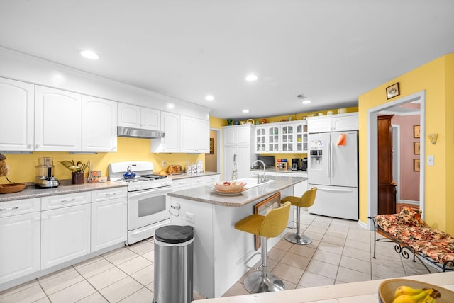 kitchen with a kitchen breakfast bar, white appliances, a kitchen island with sink, light tile patterned floors, and white cabinets