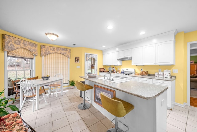 kitchen with a center island with sink, a kitchen breakfast bar, white cabinets, sink, and white gas range