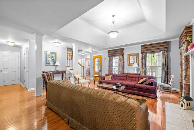 living room featuring light hardwood / wood-style floors, decorative columns, crown molding, and a tray ceiling