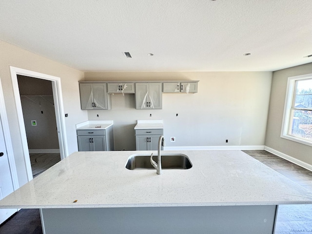 kitchen with sink, gray cabinetry, light stone counters, a center island, and a textured ceiling