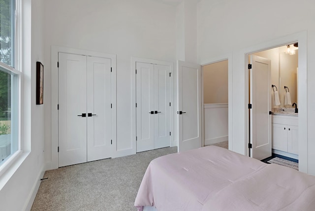 carpeted bedroom featuring a towering ceiling, two closets, multiple windows, and ensuite bathroom