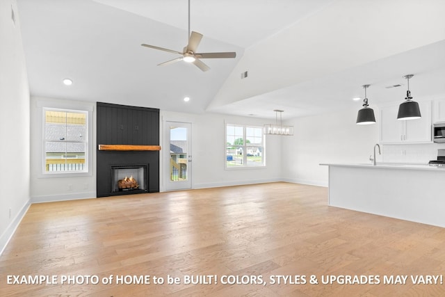 unfurnished living room featuring ceiling fan with notable chandelier, a large fireplace, a healthy amount of sunlight, and light wood-type flooring