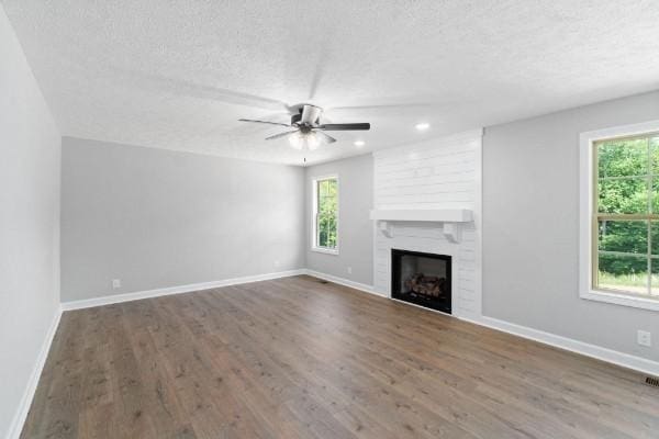 unfurnished living room with ceiling fan, a fireplace, dark wood-type flooring, and a textured ceiling