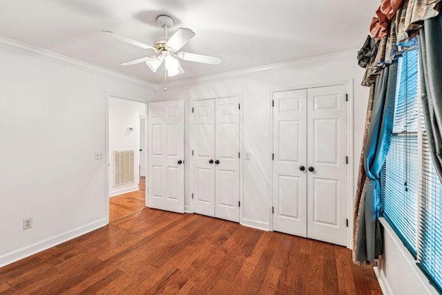 unfurnished bedroom with hardwood / wood-style flooring, ceiling fan, ornamental molding, and multiple closets