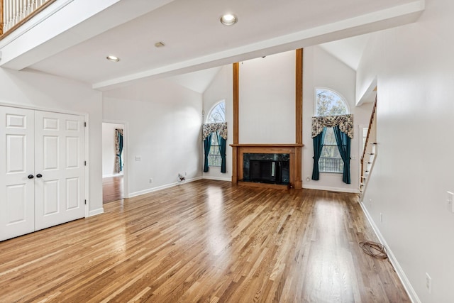 unfurnished living room with light wood-type flooring, lofted ceiling with beams, and plenty of natural light