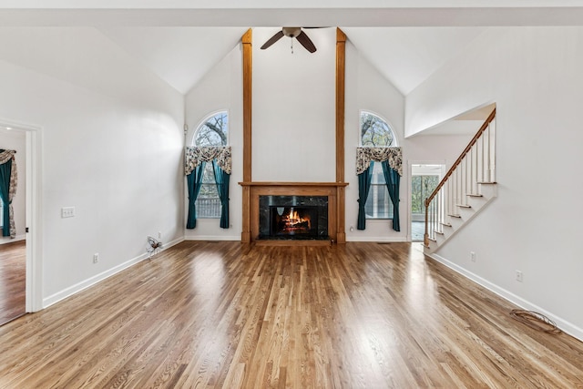 unfurnished living room featuring a fireplace, wood-type flooring, high vaulted ceiling, and ceiling fan