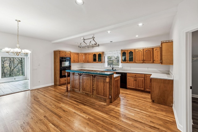 kitchen featuring light wood-type flooring, sink, black appliances, an inviting chandelier, and a kitchen island