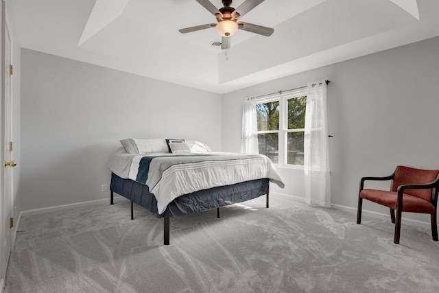 carpeted bedroom with a raised ceiling and ceiling fan