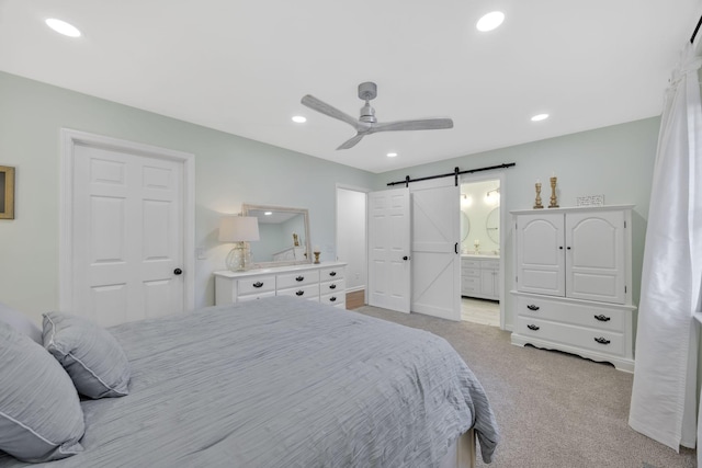 carpeted bedroom with a barn door, ceiling fan, and ensuite bathroom