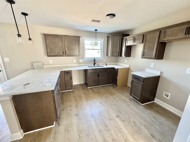 kitchen with baseboards, a peninsula, a sink, light wood-style floors, and decorative light fixtures