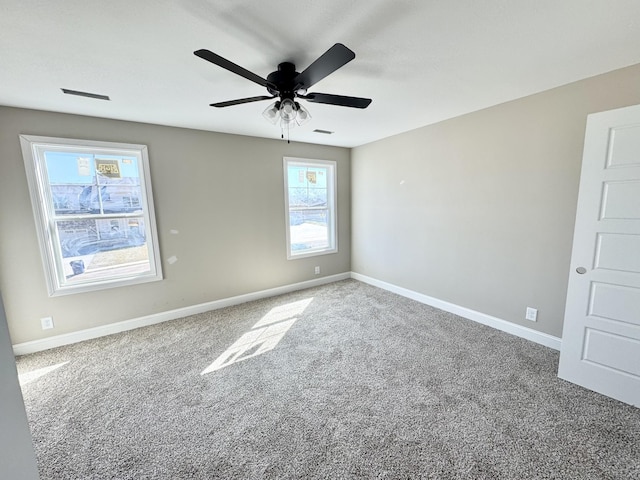 carpeted spare room with visible vents, baseboards, and ceiling fan