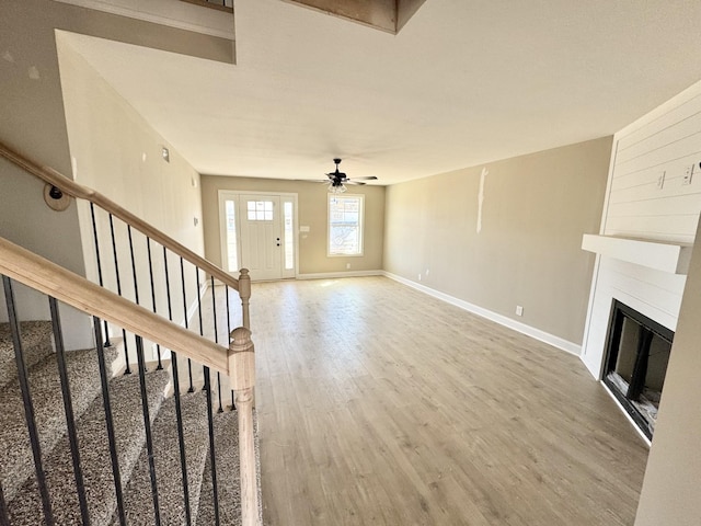 unfurnished living room featuring stairway, wood finished floors, baseboards, ceiling fan, and a glass covered fireplace