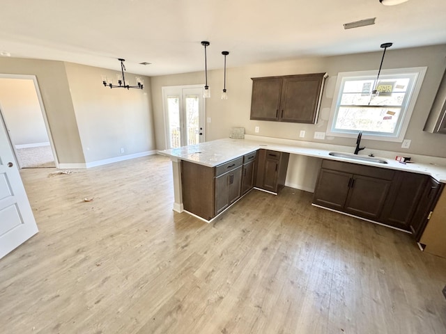 kitchen with a peninsula, a sink, dark brown cabinetry, decorative light fixtures, and light wood-type flooring