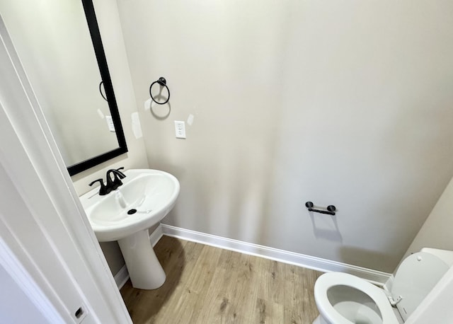 bathroom with toilet, wood finished floors, baseboards, and a sink