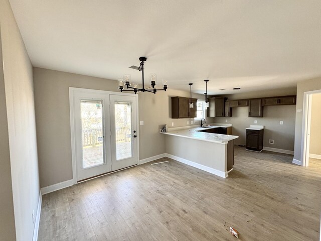 kitchen featuring light wood finished floors, an inviting chandelier, a peninsula, a sink, and dark brown cabinets