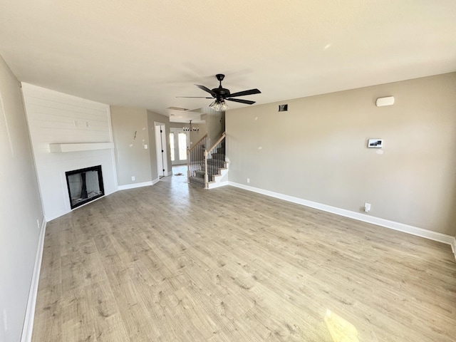 unfurnished living room featuring a large fireplace, light wood-style flooring, stairs, and baseboards