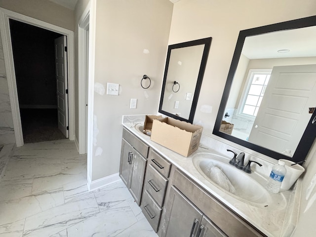 bathroom featuring a sink, baseboards, marble finish floor, and double vanity