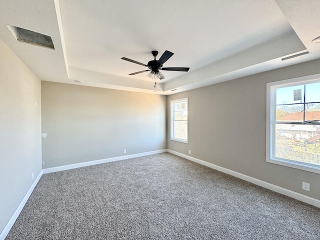 carpeted spare room with a tray ceiling, baseboards, and ceiling fan