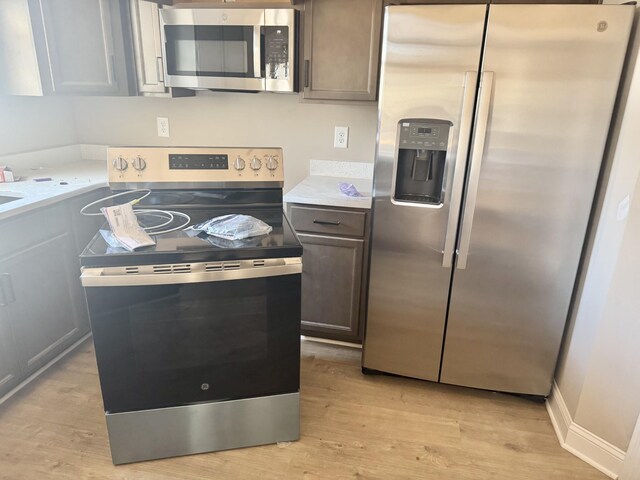 kitchen with baseboards, light wood finished floors, stainless steel appliances, dark brown cabinetry, and light countertops