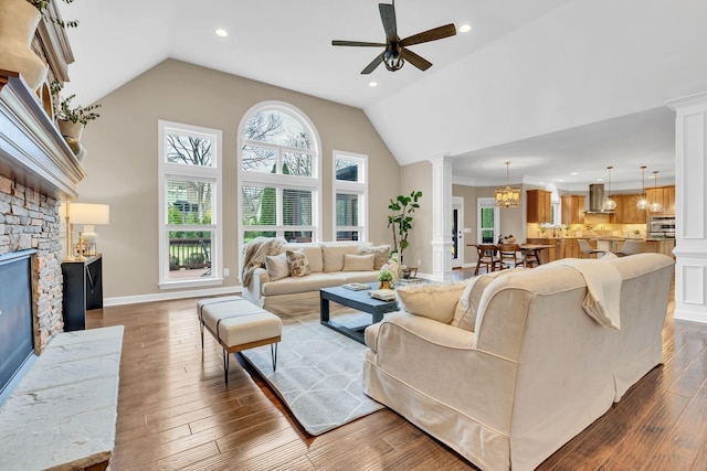 living room featuring decorative columns, dark hardwood / wood-style flooring, high vaulted ceiling, and ceiling fan with notable chandelier