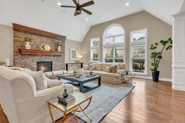 living room with ceiling fan, a stone fireplace, high vaulted ceiling, and light hardwood / wood-style flooring