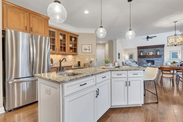 kitchen with sink, hanging light fixtures, stainless steel fridge, a kitchen island, and white cabinetry