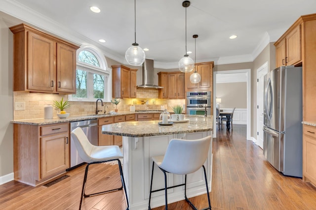 kitchen with pendant lighting, a kitchen island, stainless steel appliances, and wall chimney range hood