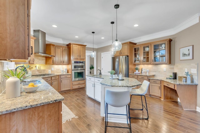 kitchen with a center island with sink, light stone counters, wall chimney range hood, and stainless steel appliances