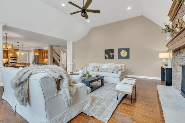 living room with lofted ceiling, ceiling fan with notable chandelier, a brick fireplace, light hardwood / wood-style floors, and decorative columns