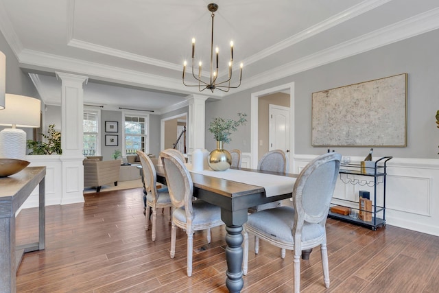 dining area with decorative columns, crown molding, a notable chandelier, and hardwood / wood-style flooring