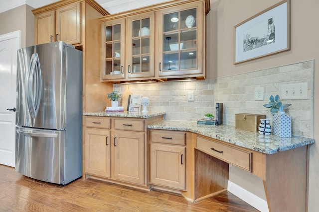 kitchen featuring stainless steel refrigerator, light stone counters, light hardwood / wood-style floors, decorative backsplash, and ornamental molding