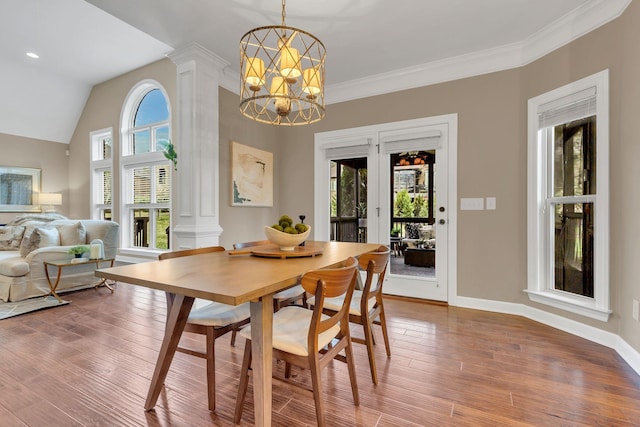 dining space with hardwood / wood-style floors, ornate columns, ornamental molding, and an inviting chandelier