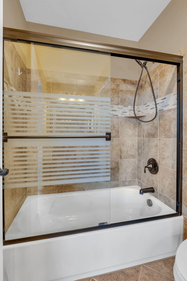 bathroom featuring tile patterned floors, toilet, and combined bath / shower with glass door