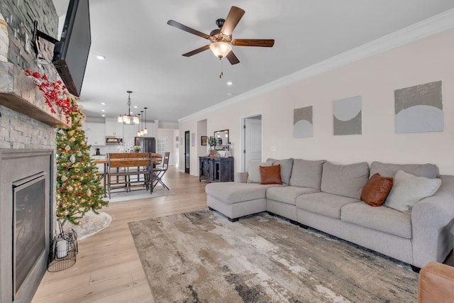 living room with ceiling fan with notable chandelier, light hardwood / wood-style floors, crown molding, and a large fireplace