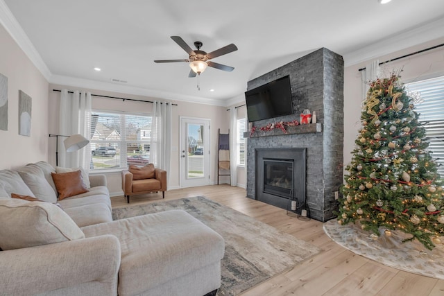 living room featuring a stone fireplace, crown molding, ceiling fan, and light wood-type flooring