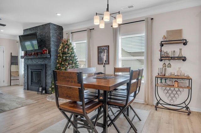 dining room with a fireplace, light wood-type flooring, crown molding, and a notable chandelier