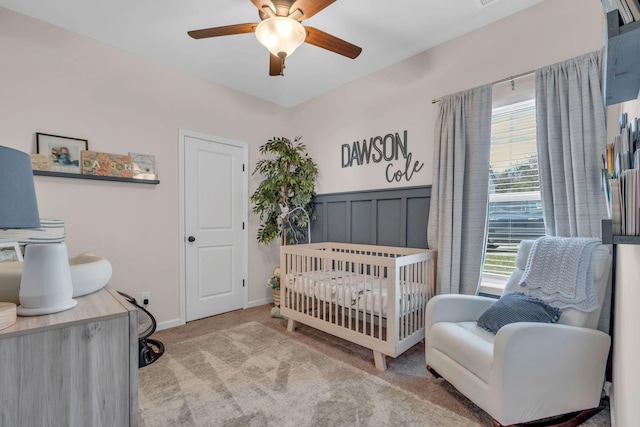 bedroom with multiple windows, ceiling fan, light colored carpet, and a nursery area