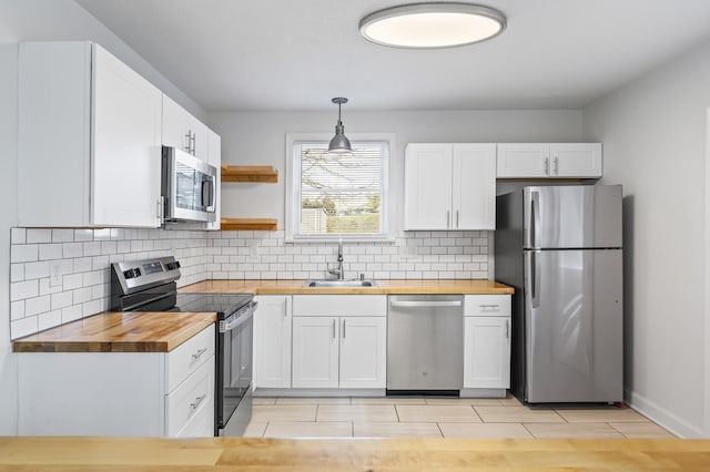 kitchen featuring white cabinetry, sink, stainless steel appliances, wood counters, and pendant lighting