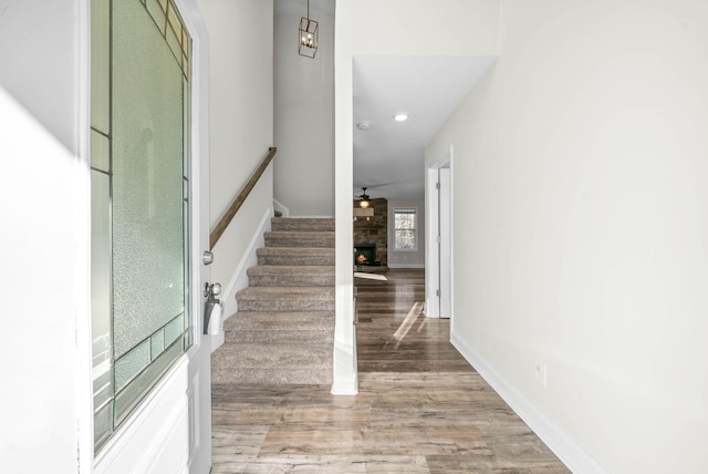 stairs featuring wood-type flooring, ceiling fan with notable chandelier, and a stone fireplace