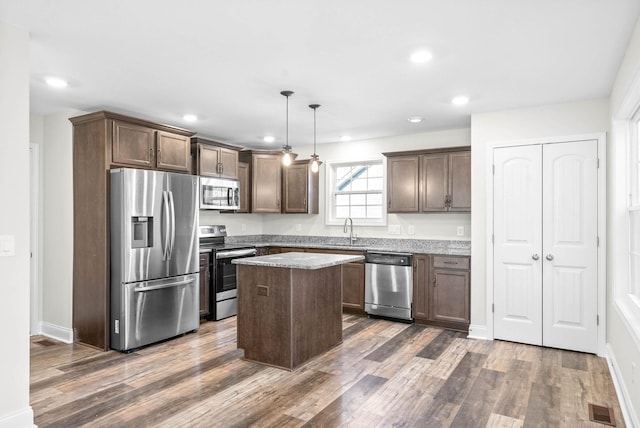 kitchen featuring sink, a center island, dark wood-type flooring, decorative light fixtures, and appliances with stainless steel finishes