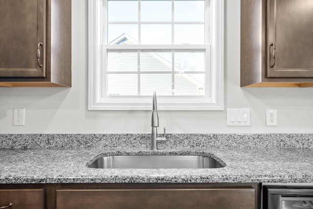 details with dark brown cabinets, light stone countertops, and sink