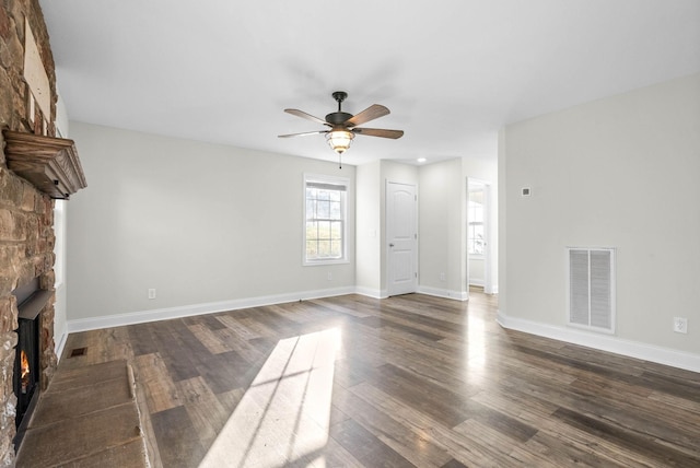 unfurnished living room featuring ceiling fan, a stone fireplace, and dark wood-type flooring