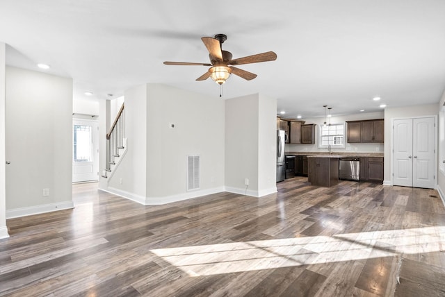 unfurnished living room featuring a wealth of natural light, sink, ceiling fan, and dark wood-type flooring