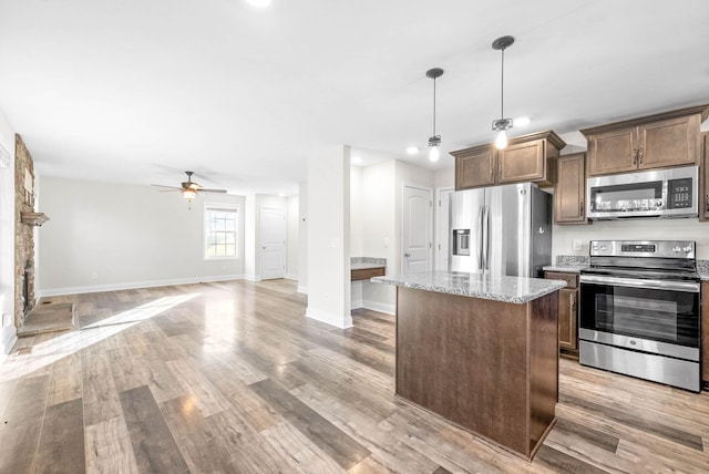 kitchen with ceiling fan, hanging light fixtures, light stone counters, appliances with stainless steel finishes, and light wood-type flooring